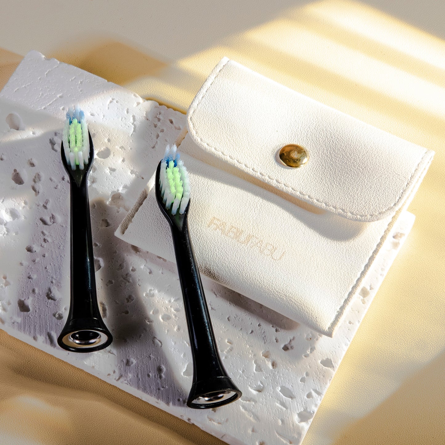 Two black electric toothbrush heads on a textured white surface with a beige pouch.